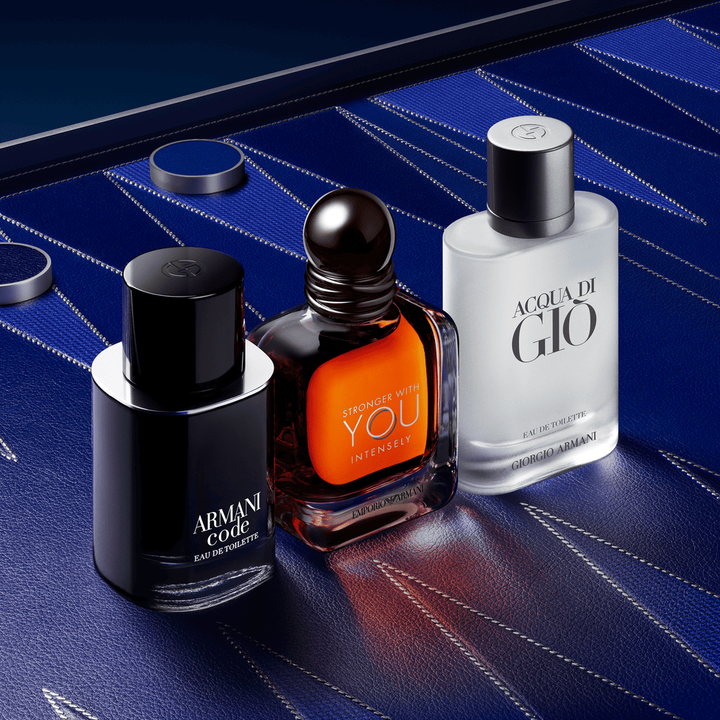 Un trio sophistique d'icones masculines : Armani Code, Stronger With You Powerfully et Acqua di Gio. Les flacons s'elevent sur un fond cuir bleu profond aux motifs geometriques couture, incarnant une elegance masculine absolue.