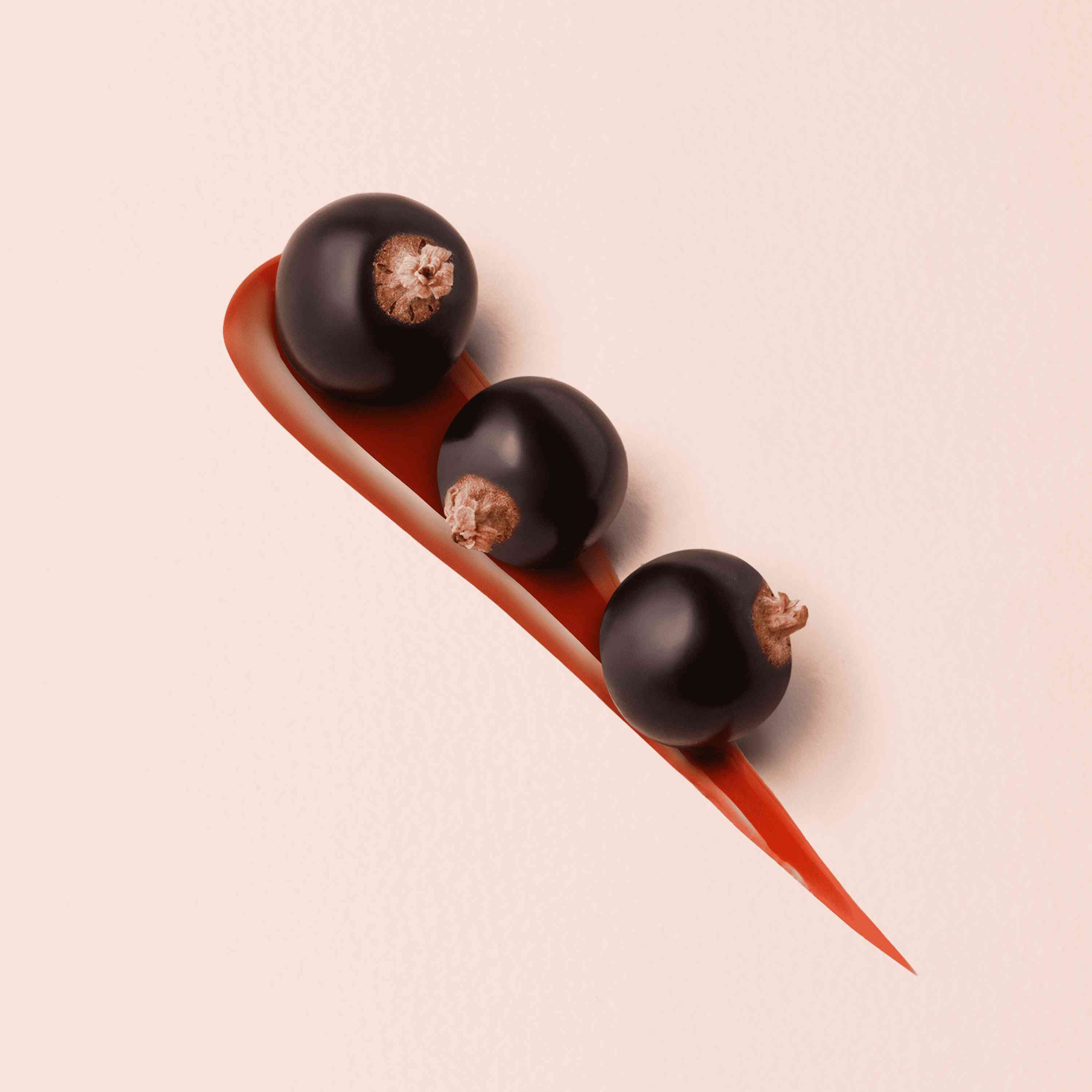 Three black currants arranged on a light background, alongside a curved smear of red fruit puree.