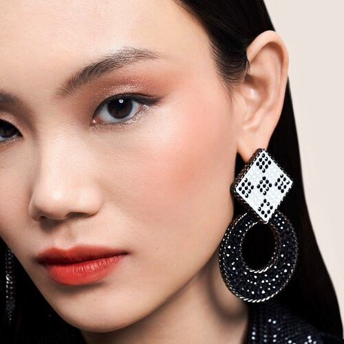 Nahaufnahme eines Modells mit schwarzen, glitzernden Ohrringen und dezentem Makeup. Der Fokus liegt auf ihrem Gesicht und den Ohrringen.