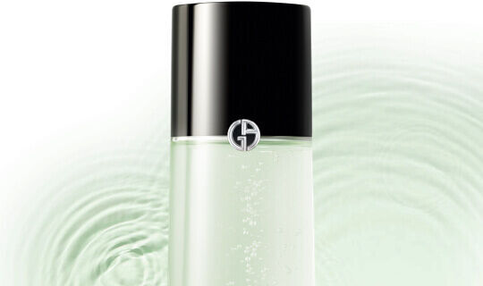 Flacon de soin avec un capuchon noir et un logo argente, sur un fond aux nuances vertes evoquant de l'eau.