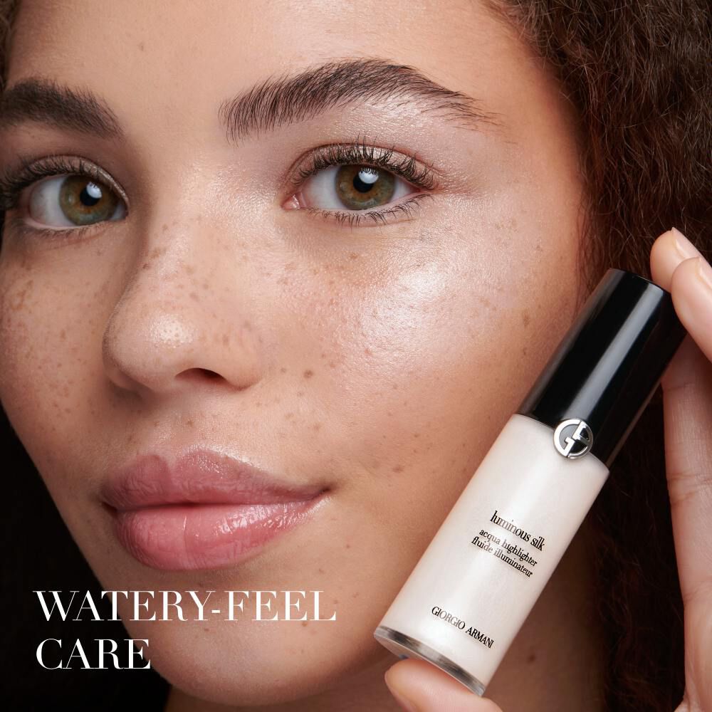 A close-up of a woman's face featuring glowing skin and freckles, holding a small bottle of Giorgio Armani skincare product. The text "WATER-Y FEEL CARE" is displayed at the bottom.
