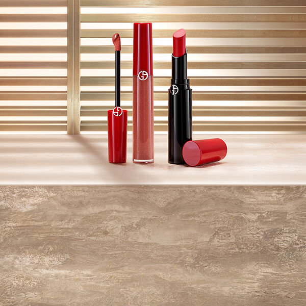 Rouge a levres liquide rouge et rouge a levres rouge Giorgio Armani, presentes sur une surface en pierre devant des stores baignes de soleil.