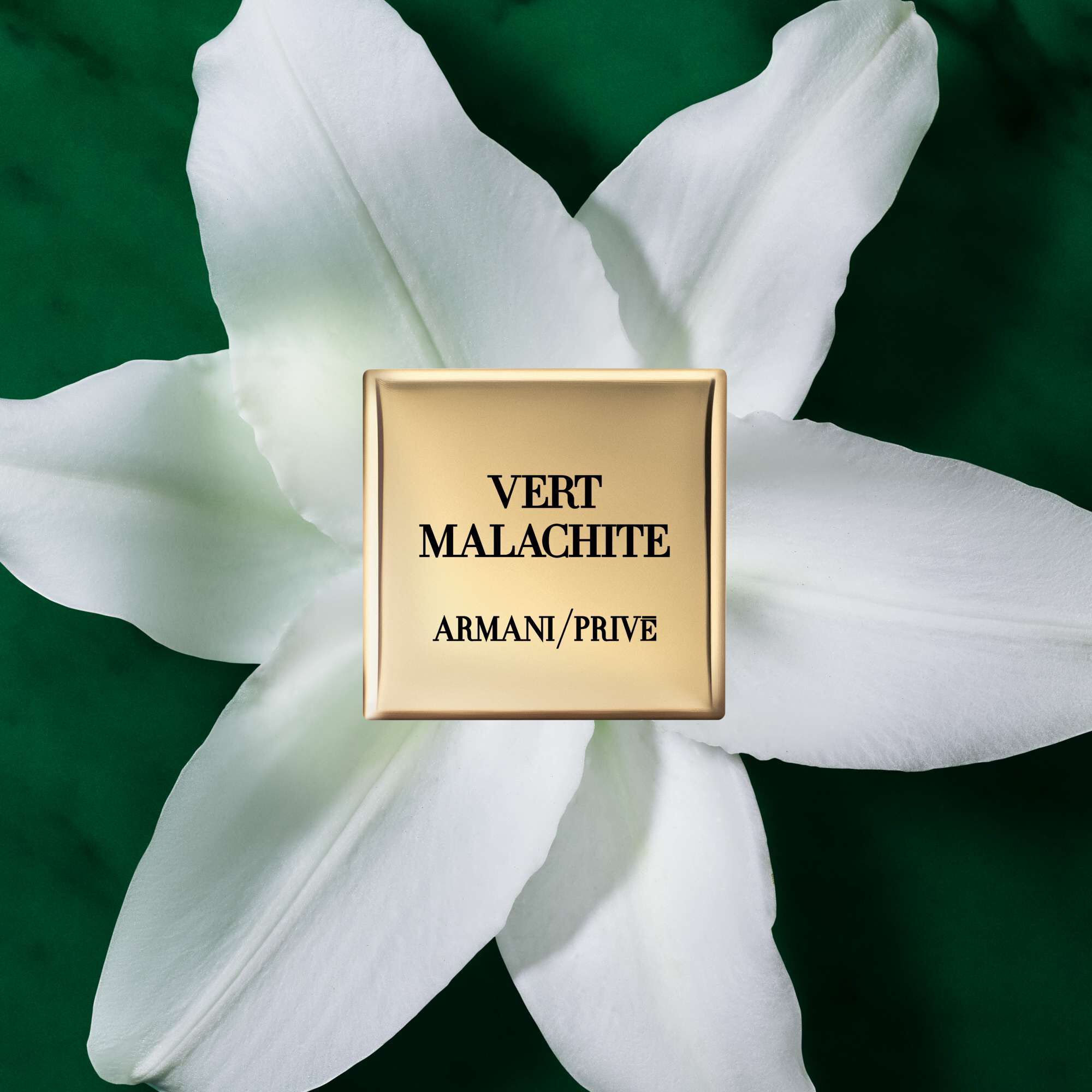 A gold rectangular perfume bottle labeled "VERT MALACHITE" from ARMANI/PRIVE, placed on a large white flower against a green background.