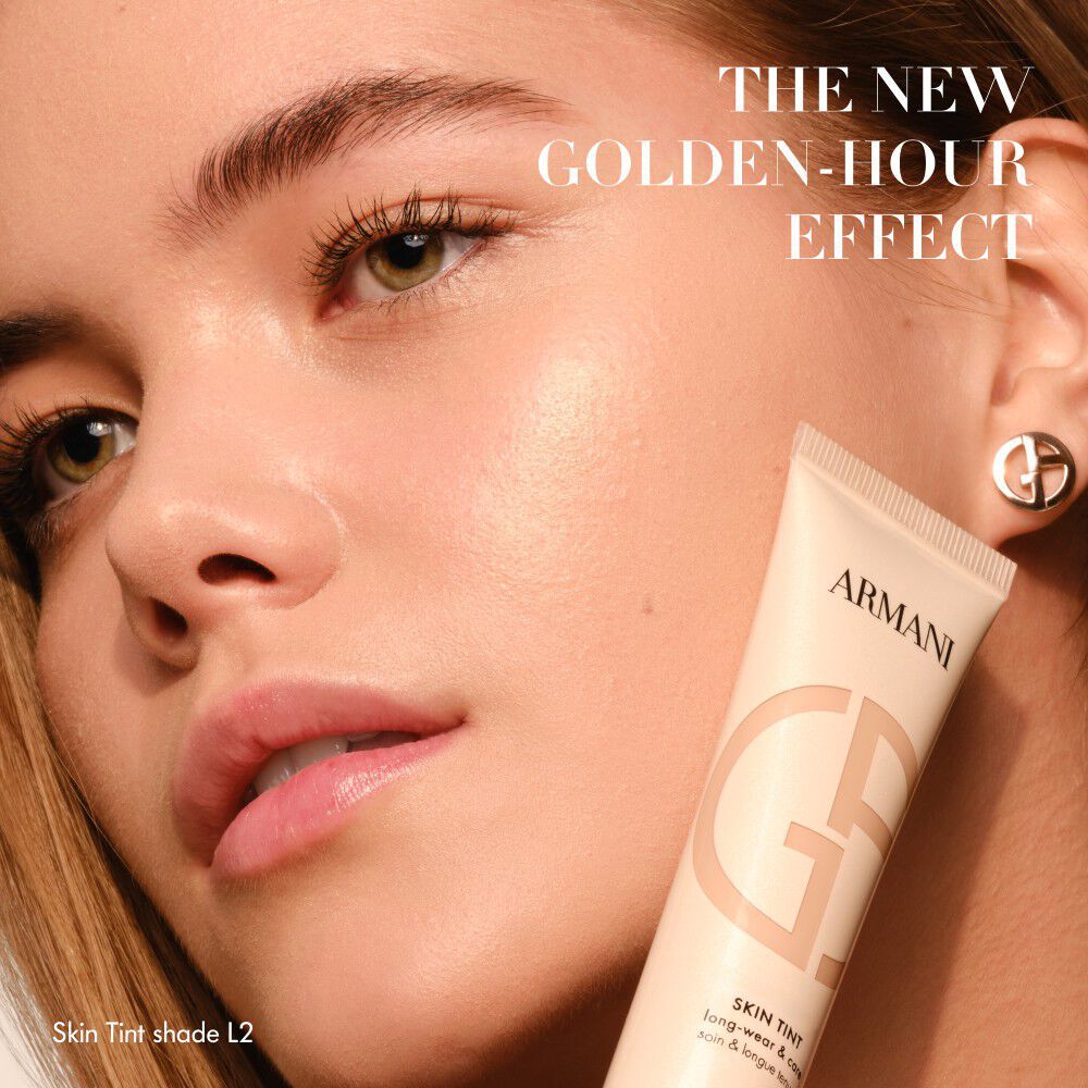 Femme a la peau eclatante tenant un tube d Armani Skin Tint, avec le texte THE NEW GOLDEN-HOUR EFFECT.
