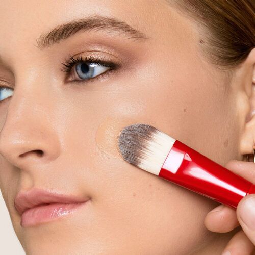 A close-up of a person's face with a makeup brush applying foundation on the cheek, displaying a natural skin look and accentuated features.