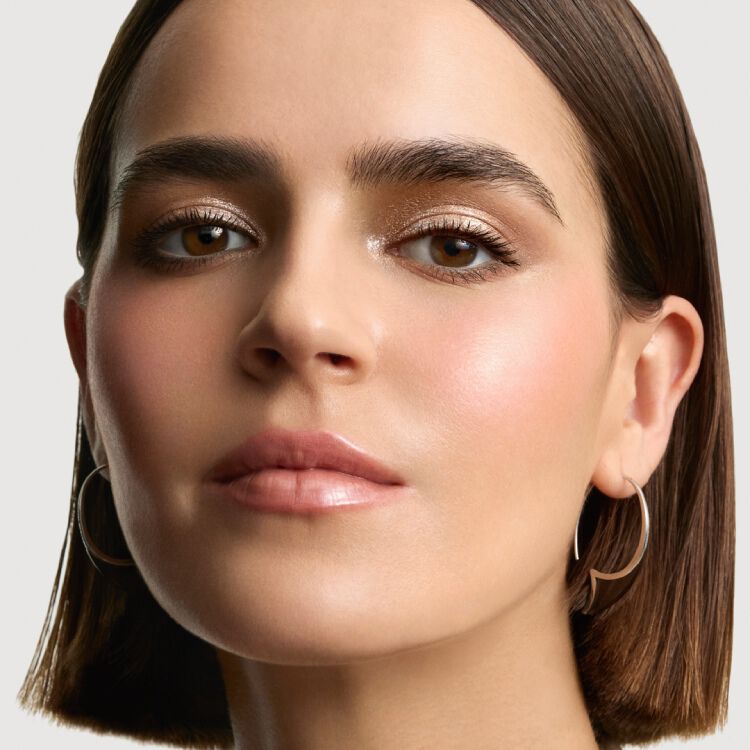 Close-up of a woman's face with natural makeup, light eyeshadow, and glossy lips, looking directly at the viewer.