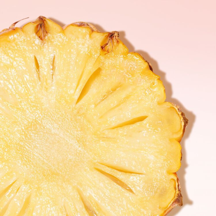 Close-up of a juicy, fresh pineapple slice on a soft pink background.