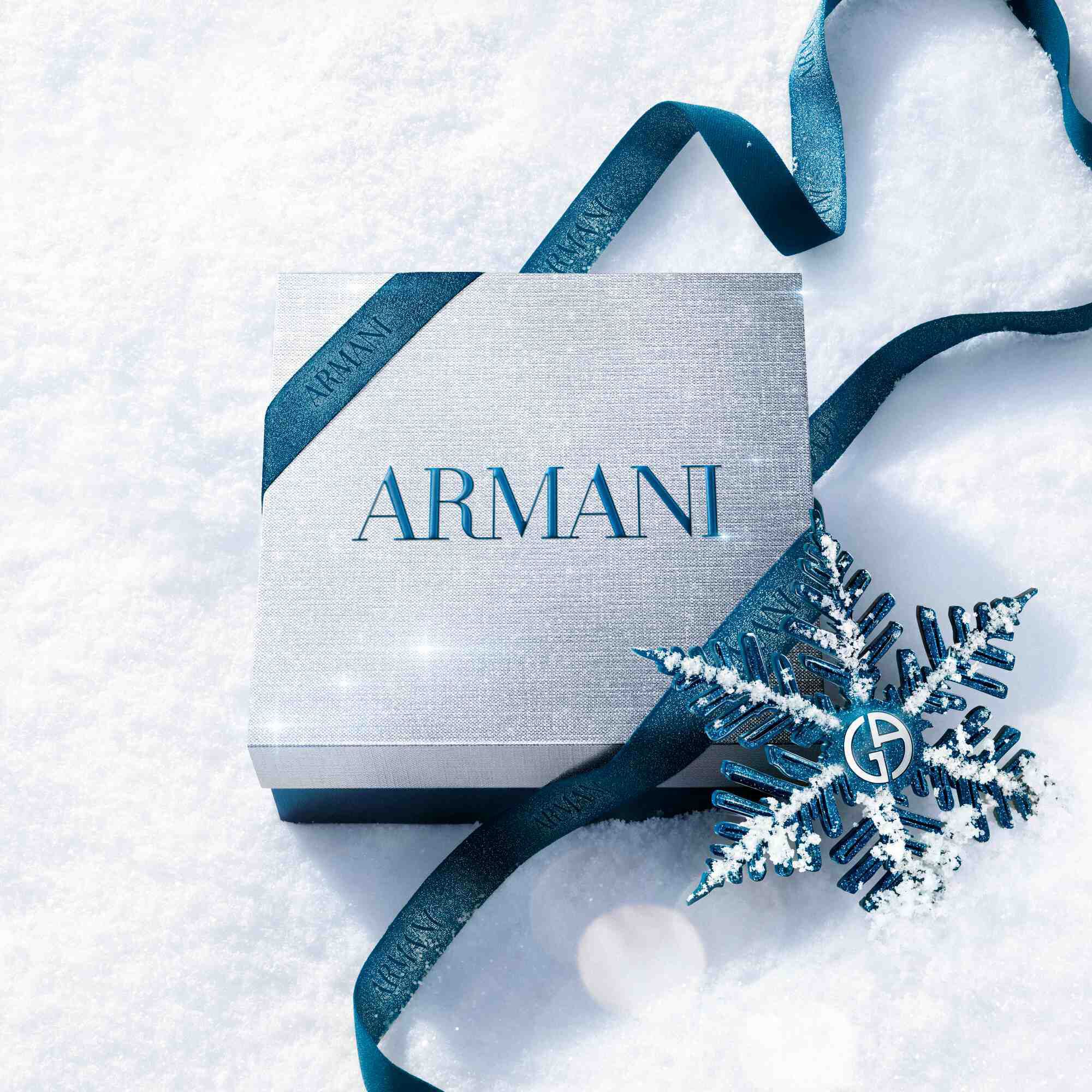 Black and amber Armani gift box with teal ribbon on a snowy surface — I Will Eau de Parfum men's fragrance gift set, holiday gifting visual.