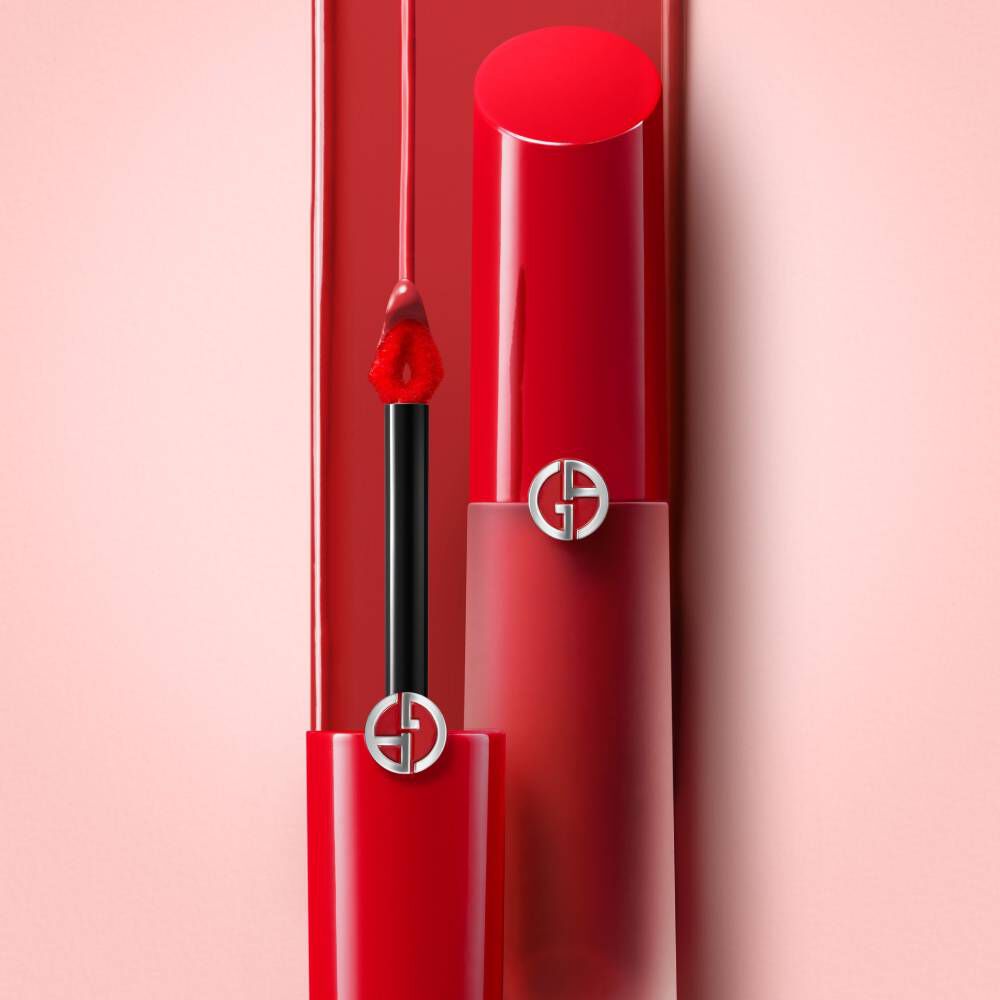 A vibrant red lipstick with a sleek applicator, partially open, resting against a soft pink background.