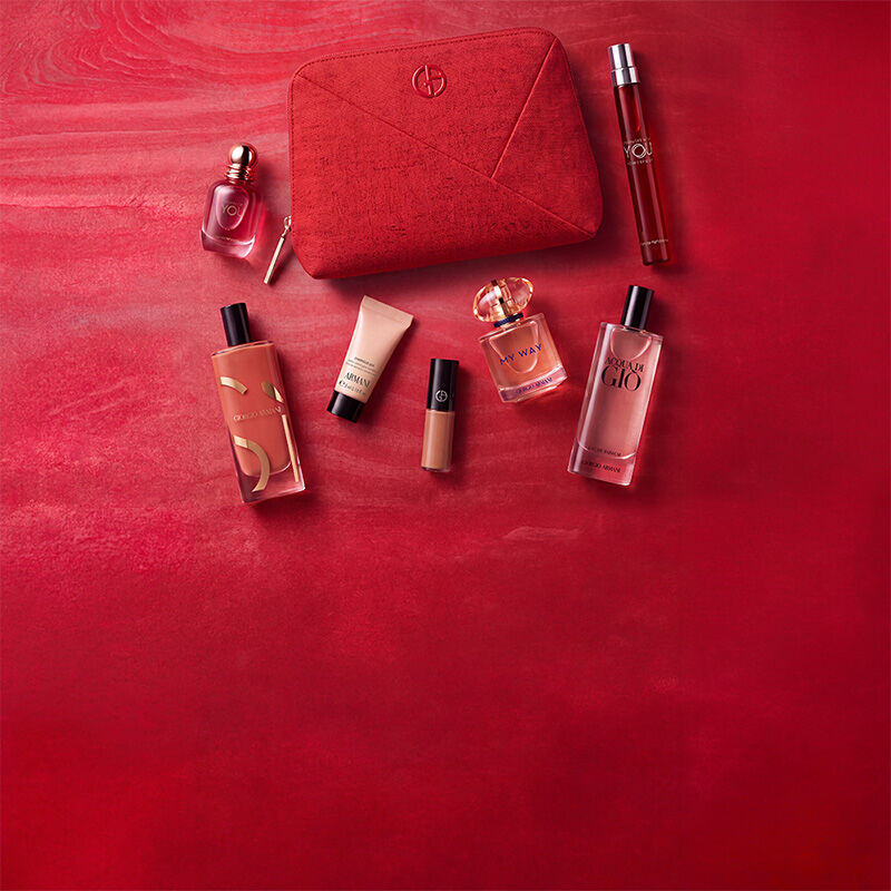 Trois produits Armani Beauty — un produit pour les levres, la fragrance Power of You et le fond de teint Luminous Silk — presentes sur un fond rouge texture.