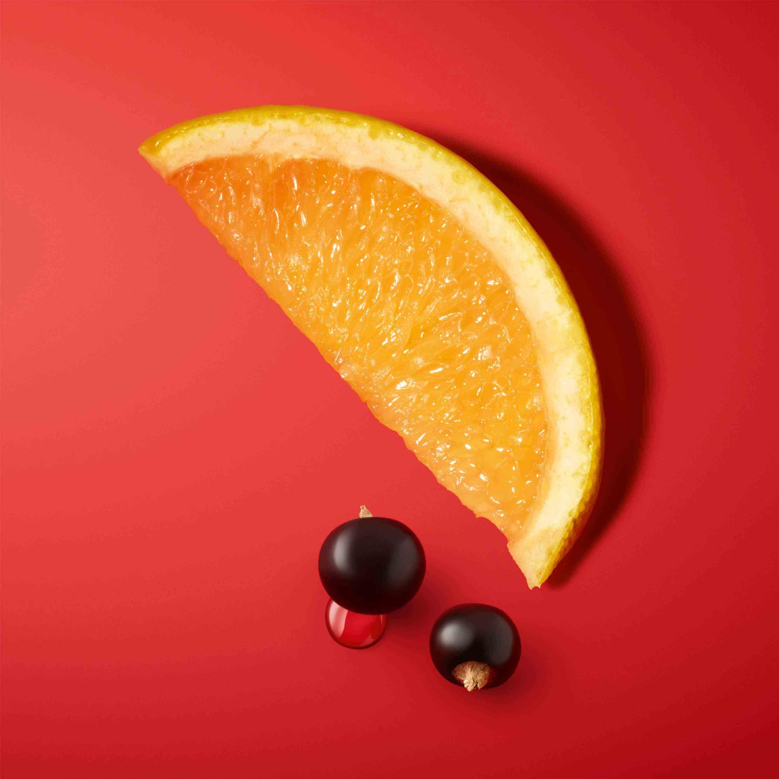 A slice of orange and two small berries, one black and one red, on a bright red background.