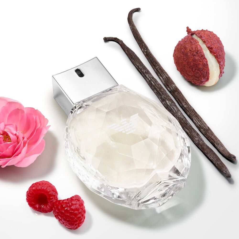 The diamond-faceted bottle of Emporio Armani "Diamonds She" fragrance is surrounded by ingredients including vanilla beans, lychee fruit, a pink rose, and raspberries.