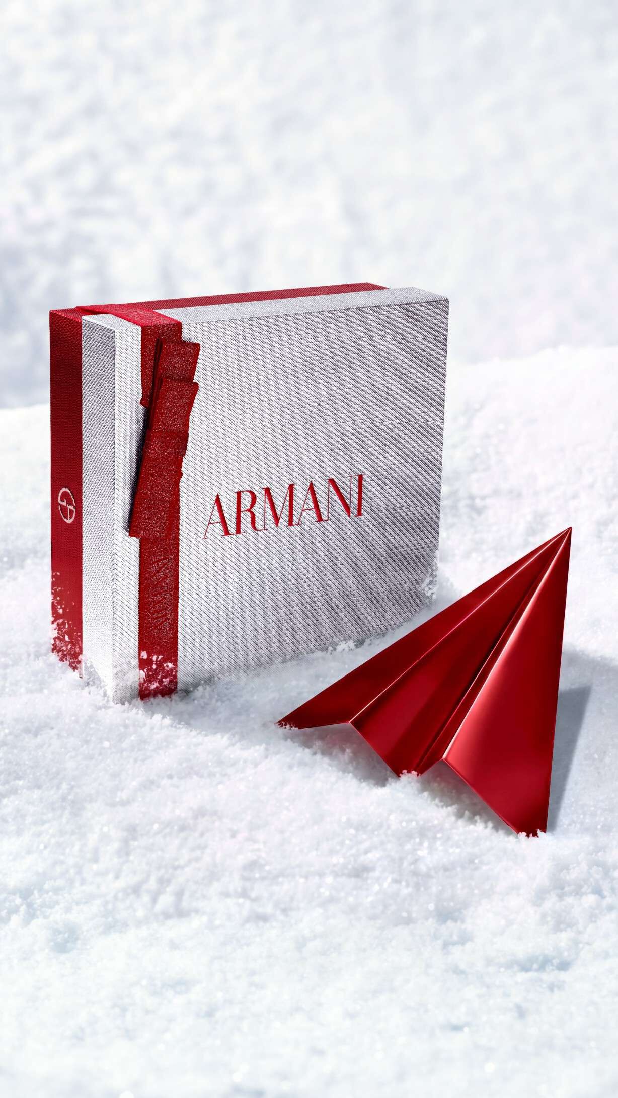 Coffret cadeau argente Armani Beauty accompagne d’un avion en papier rouge, illustrant la livraison offerte pour les fetes.