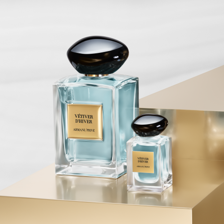 Armani/Prive: un flacon iconique et sa miniature elegante revelant une essence vert pale. Poses sur un socle dore eclatant, ils celebrent l'equilibre serein du the et le luxe artisanal de la Maison Armani.