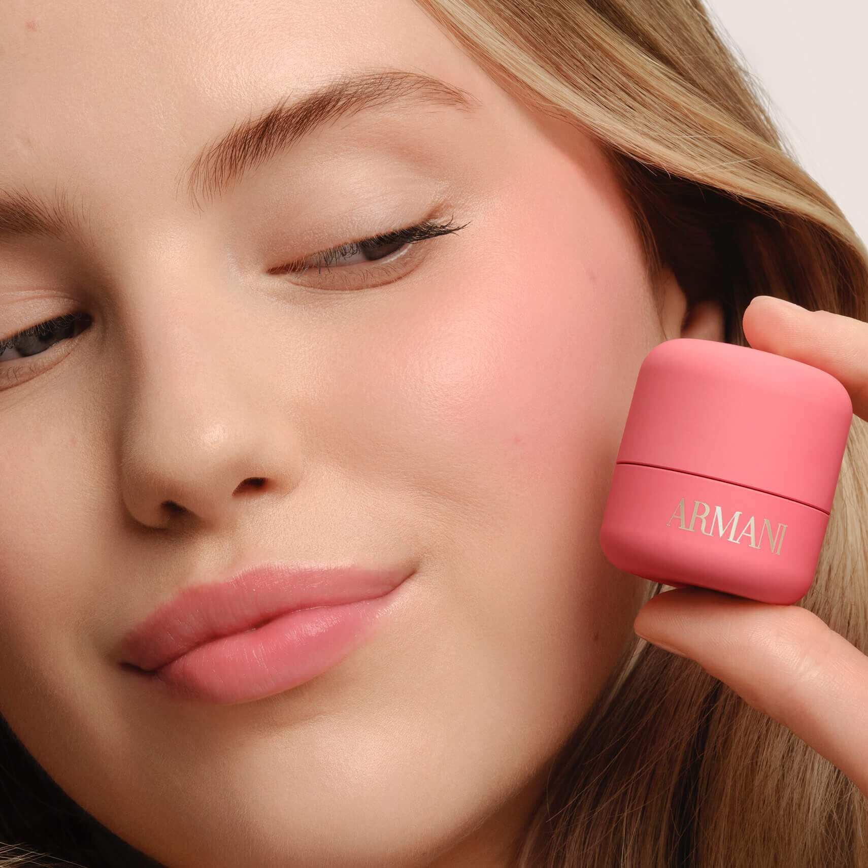 Model holding ARMANI Beauty DOLCI blush near her cheek, showing a fresh pink blush result