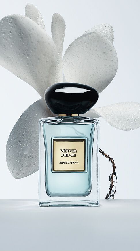Armani/Prive Vetiver d'Hiver: ein Glasflakon mit hellblauem Elixier, umrahmt von zarten weißen Blutenblattern mit Morgentau, der die klare und leuchtende Frische des Winters evoziert.