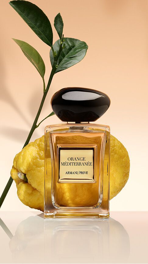 Armani/Prive Orange Mediterranee: ein Flakon mit goldenem Elixier vor einer frischen Zitrusfrucht und grunen Blattern, der die sonnenverwohnte Warme des Mittelmeers ausstrahlt.
