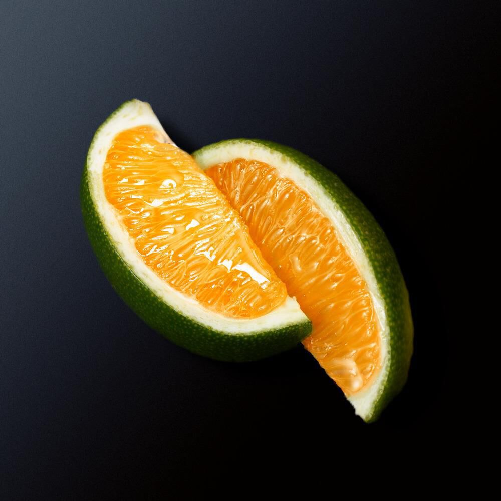 Eine halbierte Orange mit grunem Schalenrand auf schwarzem Hintergrund. Fruchtfleisch leuchtet appetitlich.