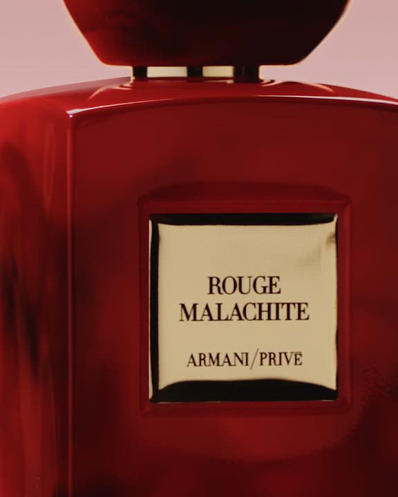 A vibrant red "Armani/Prive Rouge Malachite" fragrance bottle with a matching rounded cap. Delicate red grape clusters, white floral petals, and fiery abstract shapes softly overlay the bottle, highlighting its rich and passionate character.