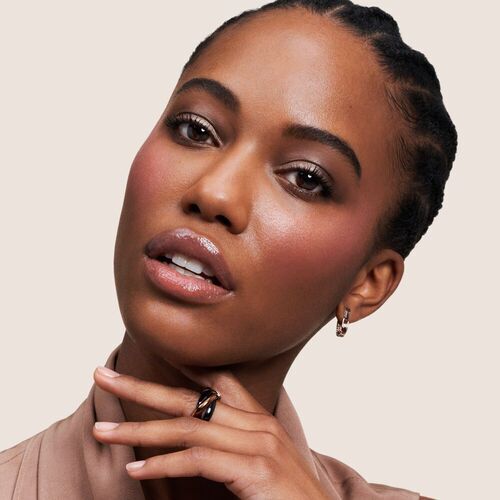 Femme au teint radieux, portant des bijoux delicats, regard direct avec un sourire subtil sur fond neutre.