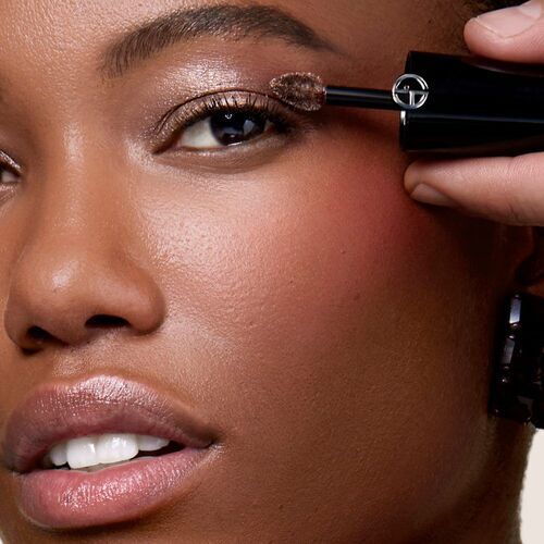 A close-up of a person applying mascara to their eyelashes, showcasing a smooth complexion and subtle makeup.