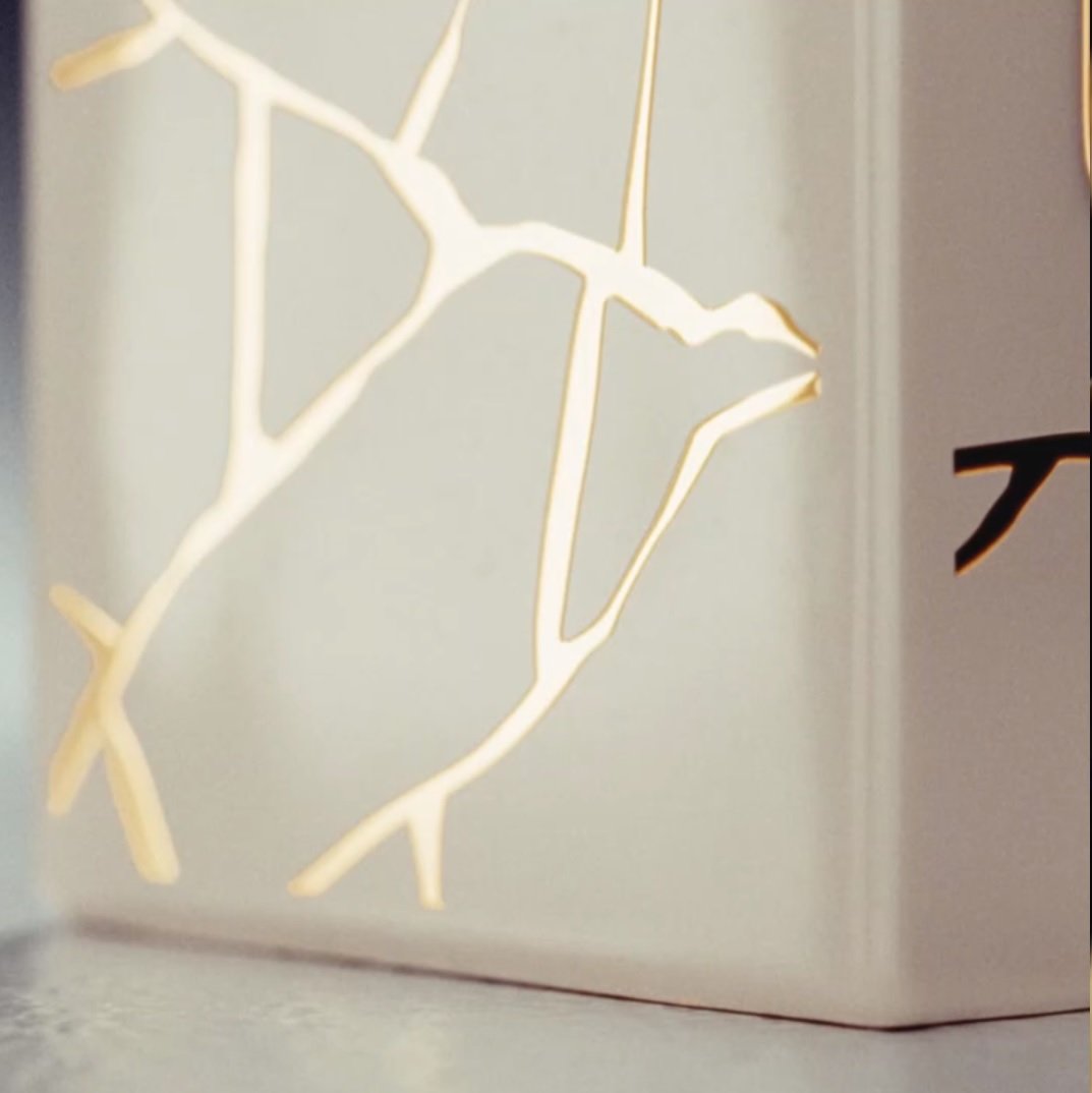 Eine stilvolle Lampe mit eleganten, goldenen Linienmuster auf weißem Hintergrund, sanft beleuchtet.